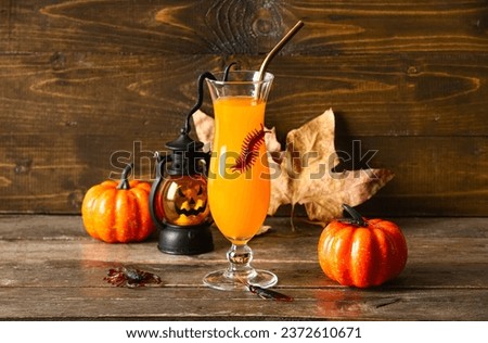 Glass of delicious orange cocktail, lantern and pumpkins for Halloween celebration on wooden background