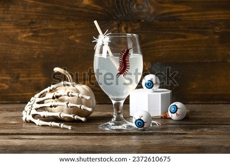 Glass of delicious cocktail, eyes and skeleton hand for Halloween celebration on wooden background