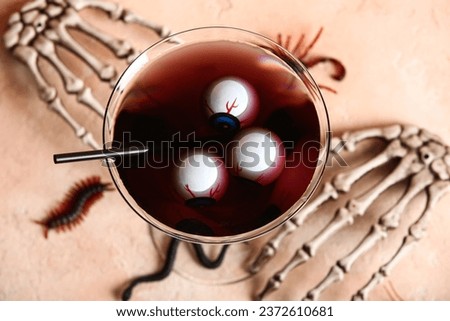 Glass of delicious cocktail, eyes, skeleton hands and candy bugs for Halloween celebration on beige background, closeup