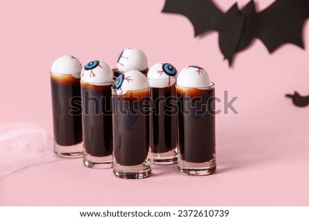 Shots of delicious cocktail and eyes for Halloween celebration on pink background