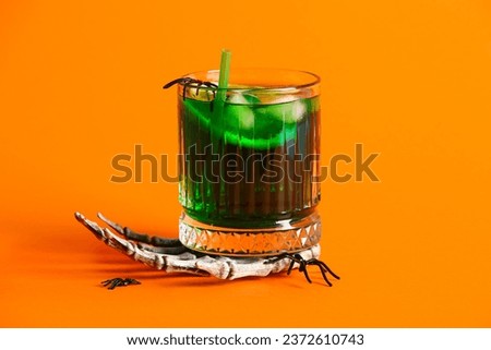 Glass of delicious green cocktail and skeleton hand for Halloween celebration on orange background, closeup
