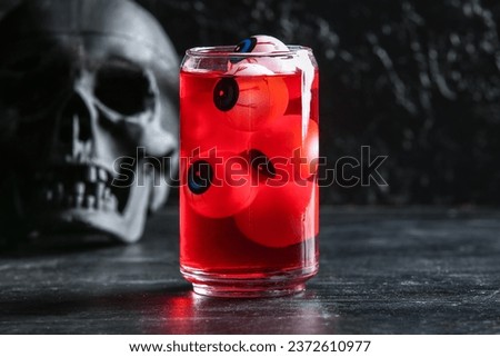 Glass of delicious red cocktail with eyes and skull for Halloween celebration on dark background, closeup