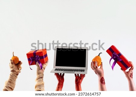 Zombie hands holding gift boxes, pumpkins and laptop with blank screen on white background. Halloween celebration