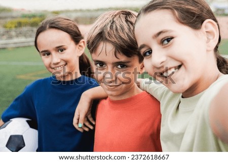 Kid friends after soccer play game having fun taking selfie in lawn - Latin children celebrating and hugging together - Childhood friendship and sport life style concept