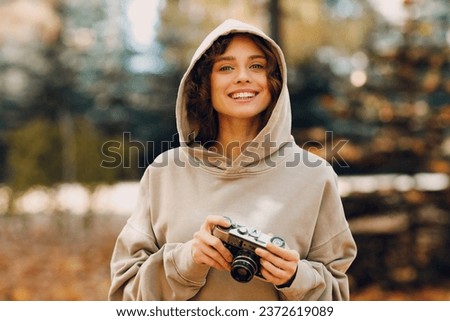 Smiling young woman with the photo camera shooting the forest trees with the yellow leaves at sunset