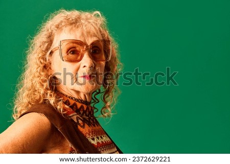 Portrait of beautiful old woman, grandmother in stylish sunglasses and accessories posing over green studio background. Concept of human emotions, fashion, elderly people, lifestyle, creativity. Ad Royalty-Free Stock Photo #2372629221