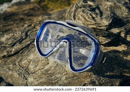 a blue diving mask lies on the rocks near the sea