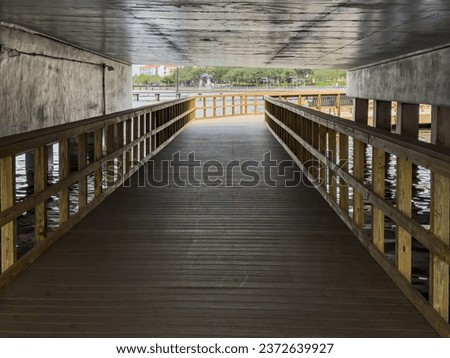 Perspective of a wooden underpass for pedestrians and bicyclists along a riverwalk on a cloudy afternoon in Bradenton, Florida, for motifs of safety and travel, tourism, and urban infrastructure