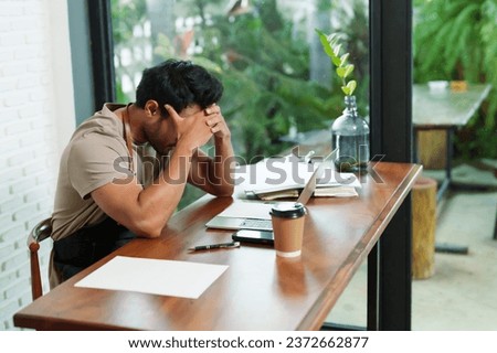 Multiethnic male business employee, cafe owner Sitting working in front tablet doing work documents next to him while holding  temples tensely disposable paper coffee cup next to. Small family cafe