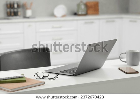 Home office. Laptop, glasses, smartphone and stationery on white desk in kitchen