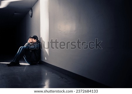 Sad man with trauma sitting on floor. Shame, guilt or sorrow. Desperate guy crying in dark corridor. Victim of loneliness or discrimination. Negative emotion or depression. Lonely outcast worrying. Royalty-Free Stock Photo #2372684133