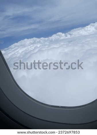 Through the airplane’s picture window, a mesmerizing view unfolds, featuring a vast expanse of thick, fluffy white clouds, stretch out as far as the eye can see, creating a serene and peaceful scene.