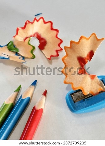 multicolored photo on a white background of 3 colored pencils with a pencil sharpener with the shavings resulting from the work done.
