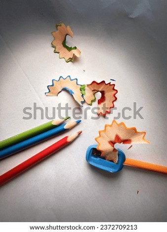 multicolored photo on a white background of 3 colored pencils with a pencil sharpener with the shavings resulting from the work done.