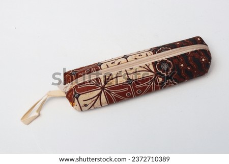 Small bag or small pouch for pencils, pens and other stationery. Equipped with a zipper. This pouch is made from patterned fabric such as batik, cream and brown. Isolated white.