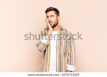young man feeling bored, frustrated and sleepy after a tiresome, dull and tedious task, holding face with hand