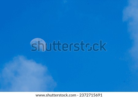 photo of the moon in the morning with a blue sky and white clouds showing brightness in the morning