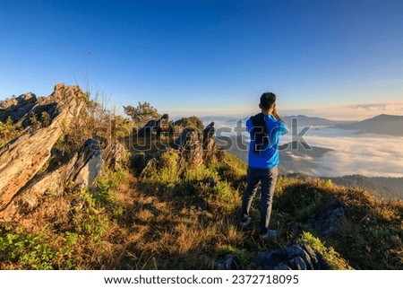 Traveler standing on the edge of the cliff holding smartphone taking a photo at the beautiful Doi pha tang mountain. Beautiful landscape sunrise mountain in Chiang rai , Northern of Thailand