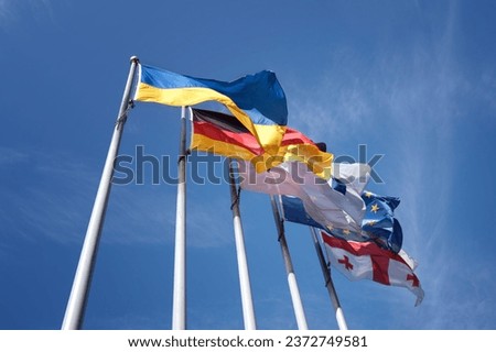 Several national flags flutter in the wind, mounted on a steel flagpole. Ukraine, Germany, European Union, Georgia. Royalty-Free Stock Photo #2372749581