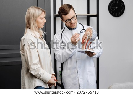 A young attractive otolaryngologist doctor shows a model of the human head and tells the patient about the structure of the respiratory system. Royalty-Free Stock Photo #2372756713