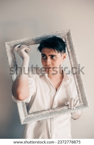 A young man in a white shirt holding an empty, beautifully ornate picture frame. The artists and their canvases. Creation art.
