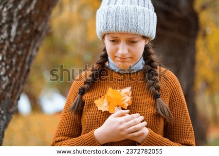 a young teenage girl posing in an autumn forest, she is unhappy and has a sad mood, standing by a tree on the riverbank, beautiful nature and bright yellow leaves
