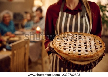 Close up of woman holding Thanksgiving pie while having a meal with her family at home. Royalty-Free Stock Photo #2372782803