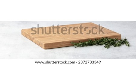 Cutting board and rosemary on a grey stone table. Isolated on a white background. Culinary background. Empty wooden cutting board, product display space. Royalty-Free Stock Photo #2372783349