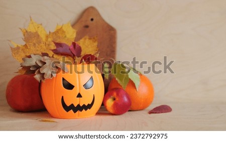 Happy Halloween. Plastic pumpkin bucket with an evil smile and autumn leaves, wooden background, pumpkins, apples and kitchen cutting board. Composition for Halloween