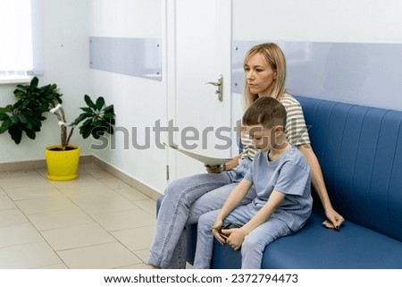 Happy toddler boy with a woman mother in the clinic waiting for a doctor s appointment. Mom with a baby boy in a modern hospital before receiving a pediatrician. Kid 5-6 year old