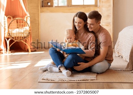 Early Education For Kids. Parents Reading Book To Their Cute Infant Son At Home, Cute Little Baby Looking With Interest, Happy Millennial Family Relaxing Together On Floor In Living Room, Free Space