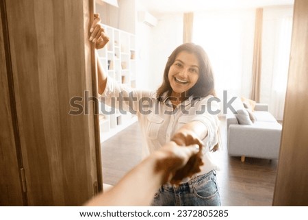 Gracious indian woman stands by open front door, extending warm handshake to guest, inviting into her cozy home with friendly and welcoming expression Royalty-Free Stock Photo #2372805285