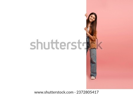 Interesting Offer. Happy Teen Girl Peeking Out Of Behind White Advertisement Board For Text Or Design, Smiling Female Teenager Holding Billboard, Looking At Camera, Standing Over Pink Background Royalty-Free Stock Photo #2372805417