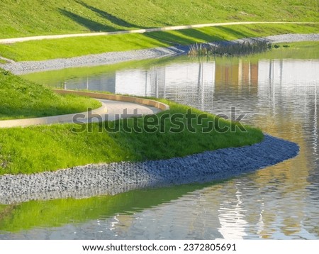 A embankment of the city pond with a green lawn and walking path. Creation of urban comfortable landscape design, urban landscape renewal. Improvement in the quality of city life. Park reconstruction