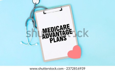 Grey stethoscope and paper plate with a sheet of white paper with text MEDICARE ADVANTAGE PLANS light blue background. Medical concept. Royalty-Free Stock Photo #2372816939