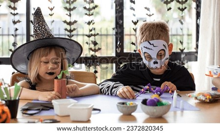 Cute brother and sister in Halloween costumes make festive crafts at the table. A master class on Halloween crafts. Happy Halloween.