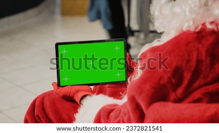 Employee in xmas ornate clothing store dressed as Santa Claus holding green screen tablet, setting up website clothing articles, inputting promotional Christmas offers online