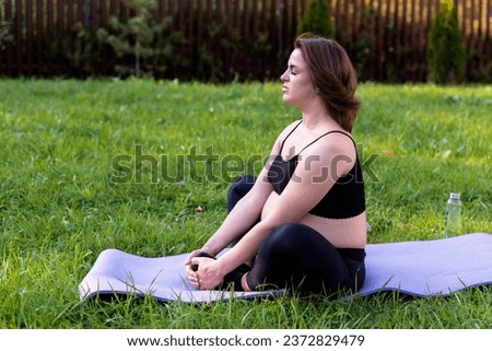 Pregnant woman doing yoga and meditating on grass in the yard, deep breath with fresh air do yoga lotus pose comfortable, yoga motherhood, mental health