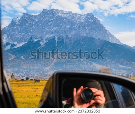 Photographer reflection in car mirror while taking picture of Austrian Alps during vacation road trip