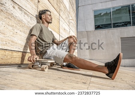 Surf skater resting sitting on his skateboard in an urban scene. Royalty-Free Stock Photo #2372837725