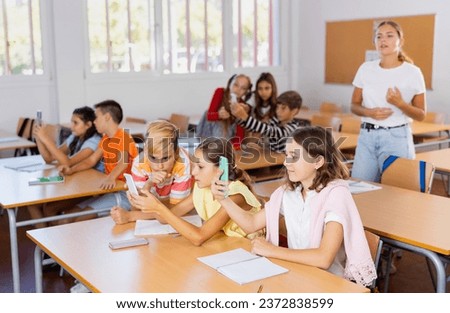 Group of kids sitting at desks in classroom during lesson and using smartphones to take pictures. Schoolkids photographing with phones.