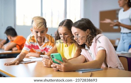 Group of kids using smartphones during lesson in school. Girls and boys using gadgets while studying. Royalty-Free Stock Photo #2372838693