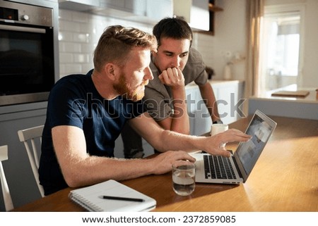 Young male gay couple browsing on the laptop together at home Royalty-Free Stock Photo #2372859085
