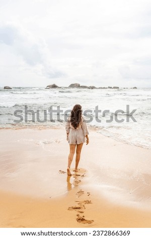 Woman in jumpsuit on beach walking towards the sea Royalty-Free Stock Photo #2372866369