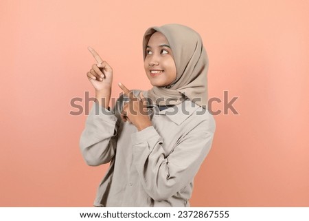 A beautiful young Asian woman is pointing upwards with both fingers while looking up while smiling showing her teeth