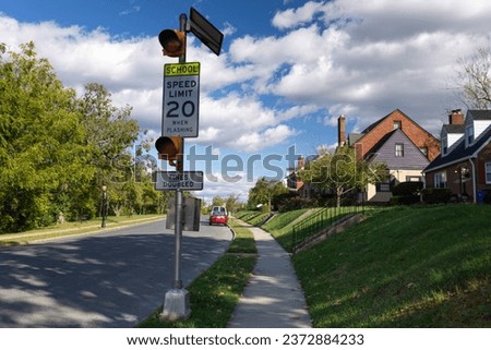 Quiet suburban street in Frederick, MD, with two-story houses, green lawns, and a school zone warning sign flashing at 20 miles per hour, emphasizing the importance of road safety