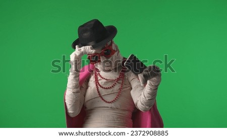 Green screen isolated chroma key photo capturing a mummy wearing pink jacket, hat and accessiores taking selfies, pictures of itself on a smartphone.