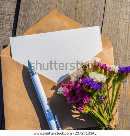 Static flowers and an envelope with an empty postcard. An empty postcard made of white paper and an envelope made of kraft paper, a letter with a place to copy the text, a greeting or an invitation. 