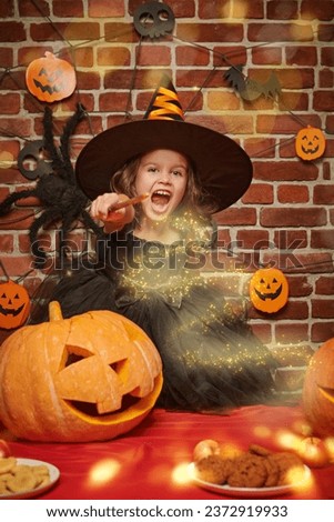 A cute little witch casts a spell with a magic wand, standing over a large pumpkin. Halloween.