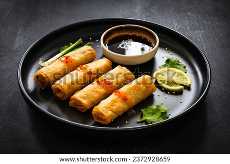 Vegetable filled spring rolls and soy sauce on black wooden table  Royalty-Free Stock Photo #2372928659